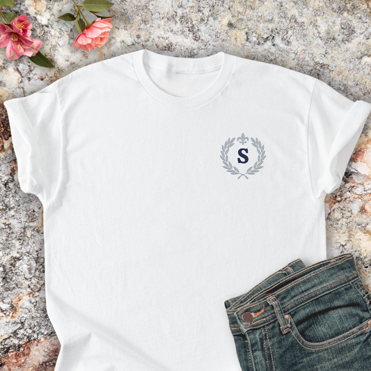 White t-shirt with a monogram design on a textured surface with jeans and flowers.
