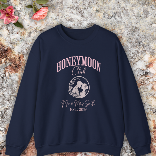 Navy sweatshirt with 'Honeymoon Club' design on a textured surface with flowers.