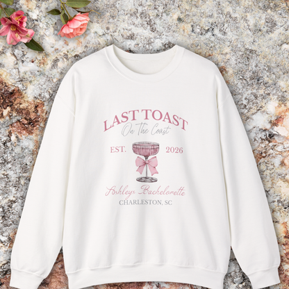 White sweatshirt with 'Last Toast on the Coast' design on a stone surface with flowers.