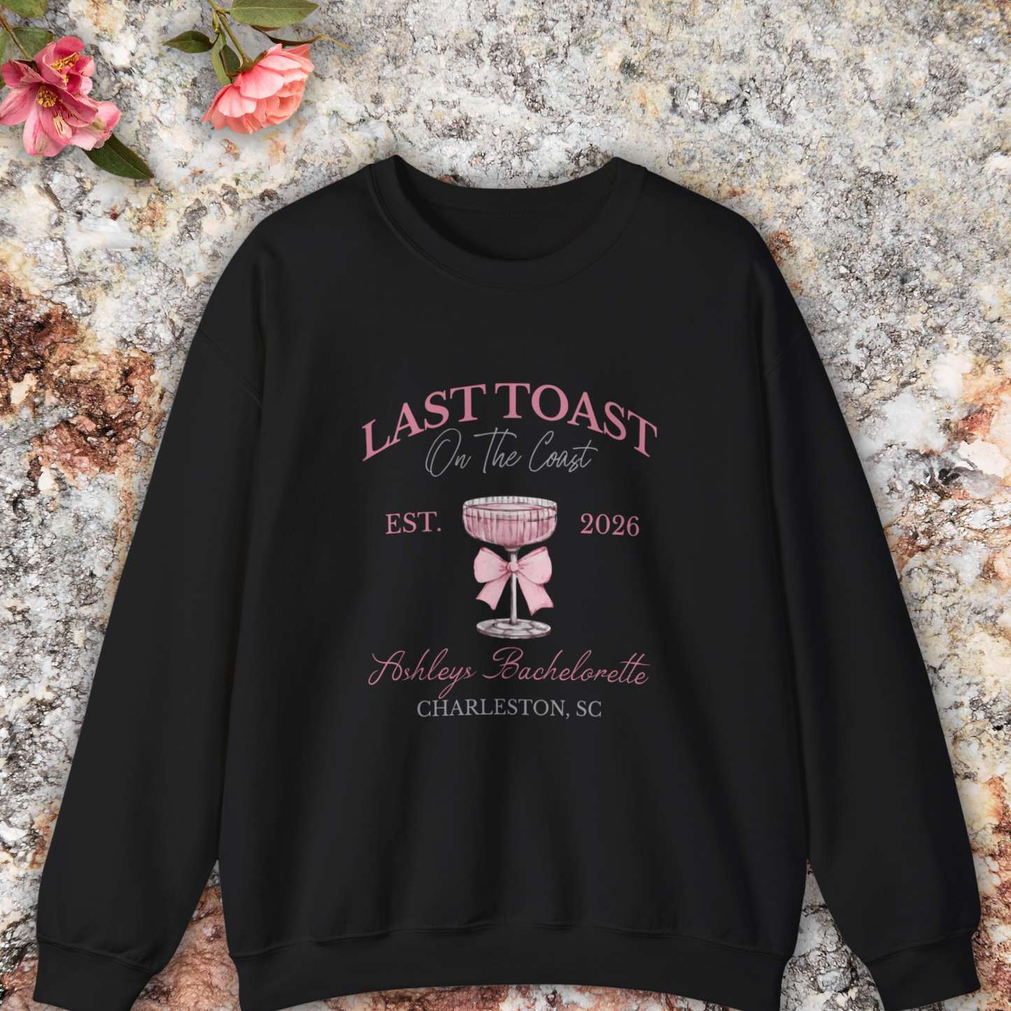 Black sweatshirt with 'Last Toast on the Coast' design on a stone surface with flowers.