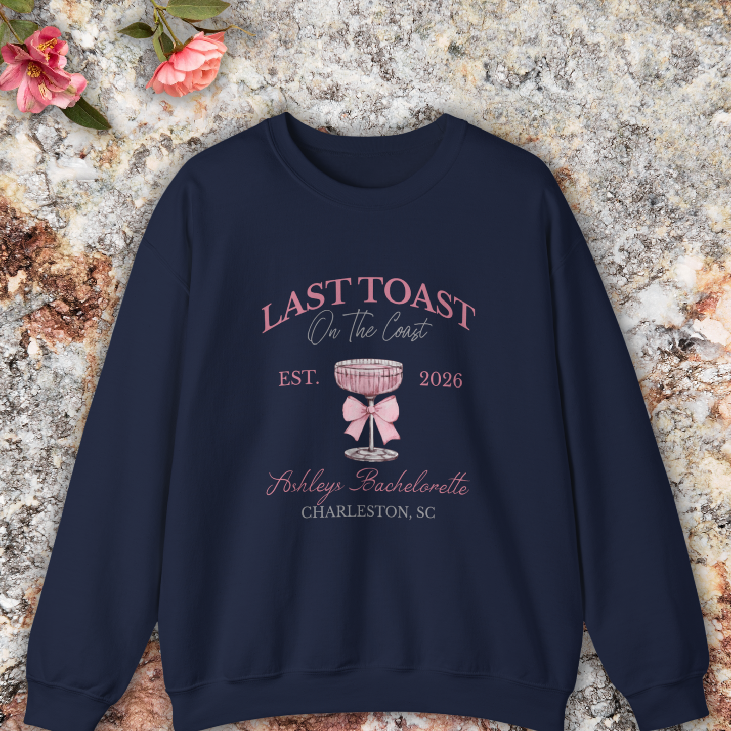 Navy sweatshirt with 'Last Toast on the Coast' design on a stone surface with flowers.