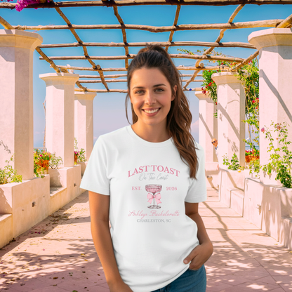 Woman wearing a white t-shirt with pink text and graphics, standing on a sunlit patio with flowers and columns.