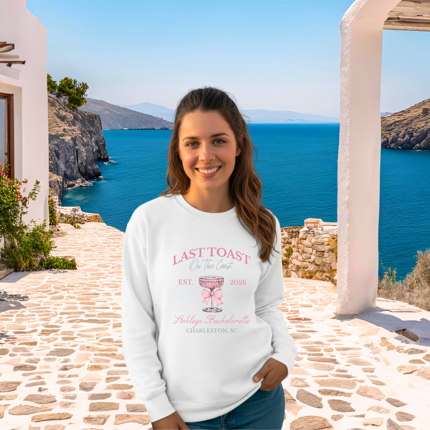 Woman wearing a white sweatshirt with text and graphics, standing in front of a scenic ocean view.