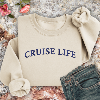 Sand sweatshirt with 'CRUISE LIFE' text on a textured surface with flowers and jeans.