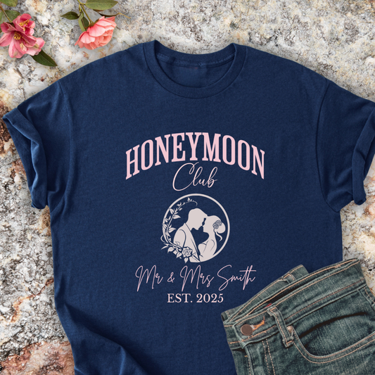 Navy shirt with 'Honeymoon Club' design on a textured surface with flowers and jeans.