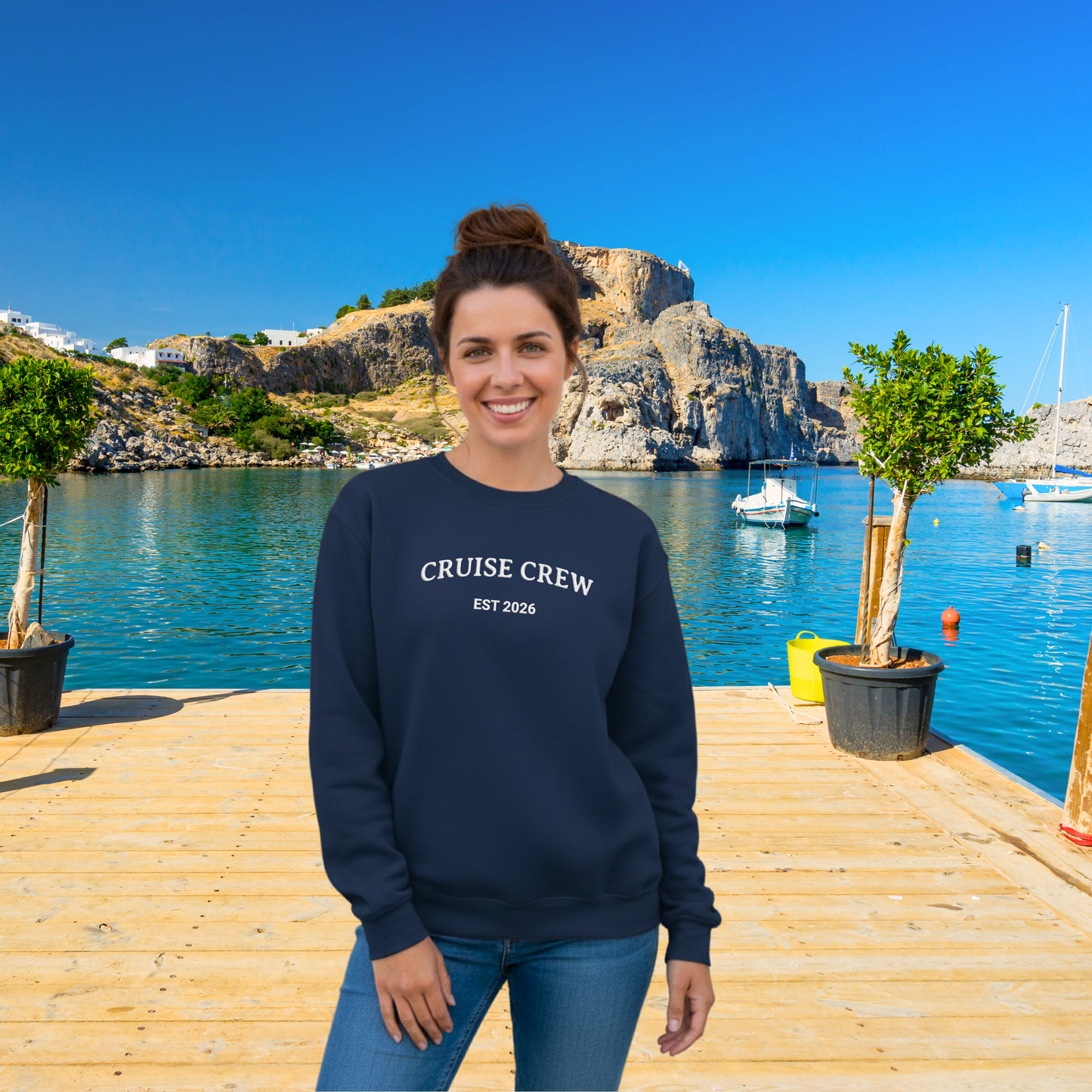 Woman wearing a navy sweatshirt with 'Cruise Crew' text, standing on a wooden dock with a scenic background.