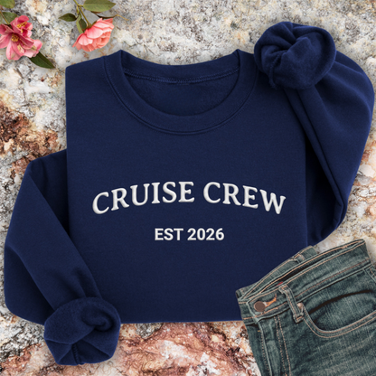 Navy sweatshirt with 'CRUISE CREW EST 2026' text on a textured surface with flowers and jeans.