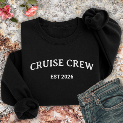 Black sweatshirt with 'CRUISE CREW EST 2026' text on a textured surface with flowers and jeans.