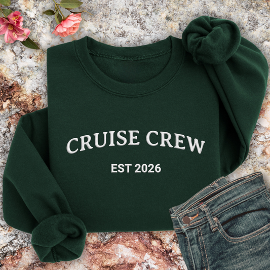 Forest Green sweatshirt with 'CRUISE CREW EST 2026' text on a textured surface with flowers and jeans.