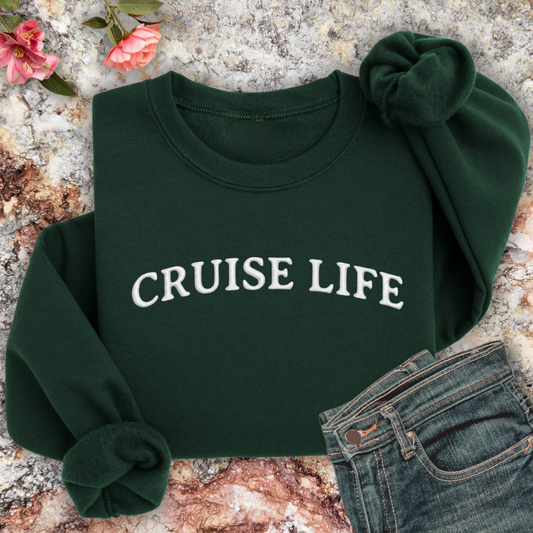 Forest Green sweatshirt with 'CRUISE LIFE' text on a textured surface with flowers and jeans.