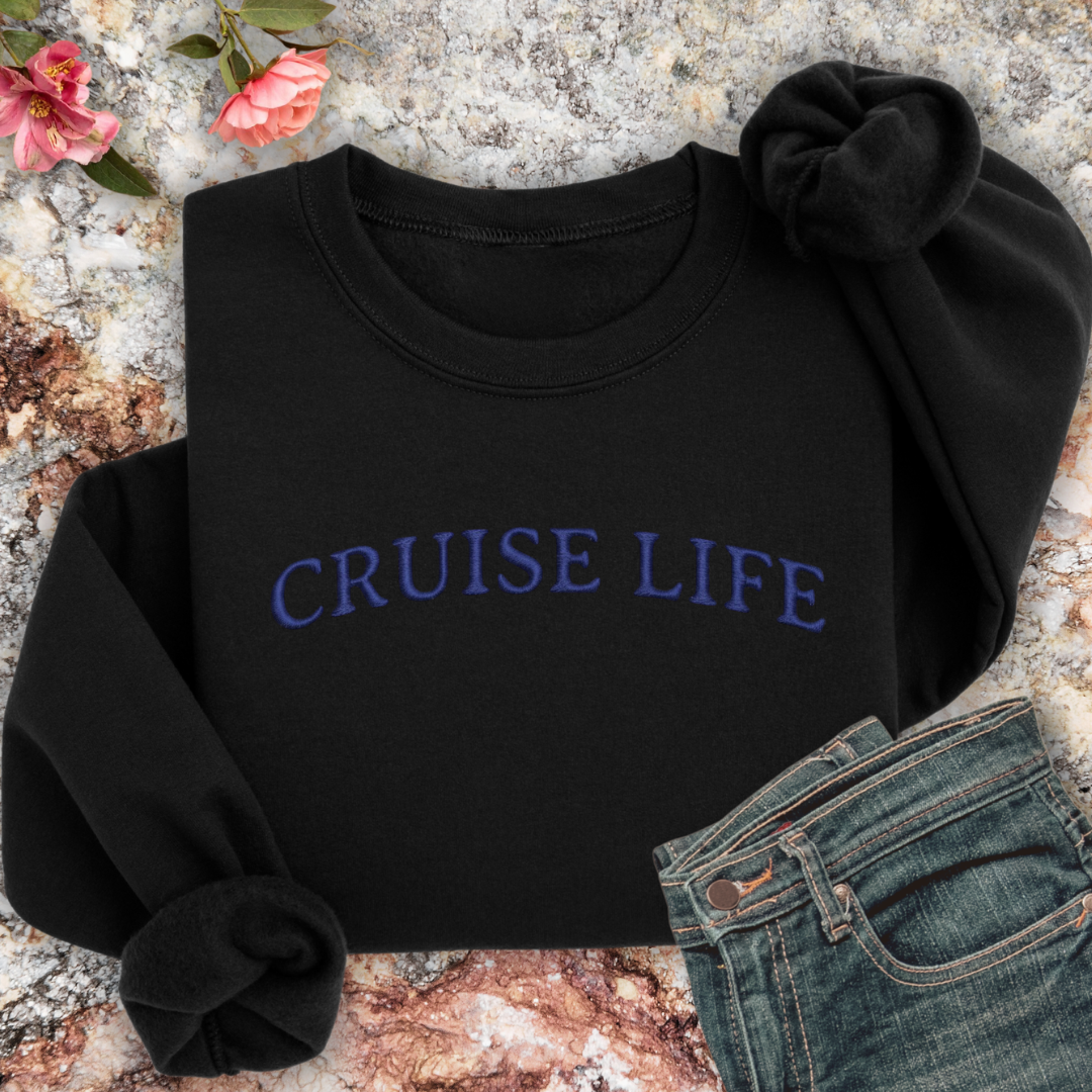 Black sweatshirt with 'CRUISE LIFE' text on a textured surface with flowers and jeans.