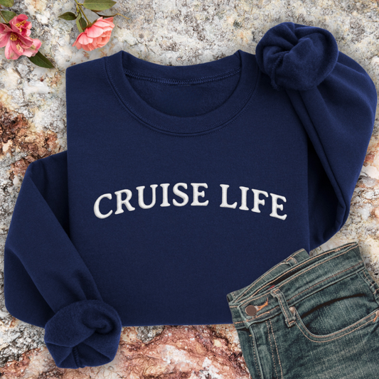 Navy sweatshirt with 'CRUISE LIFE' text on a textured surface with flowers and jeans.