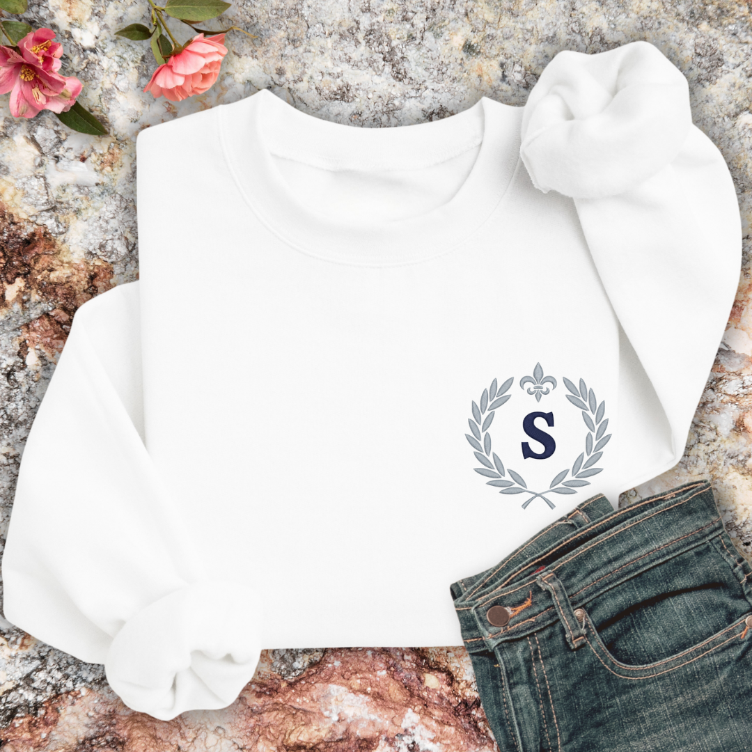 White sweatshirt with a monogram on a marble surface with flowers.